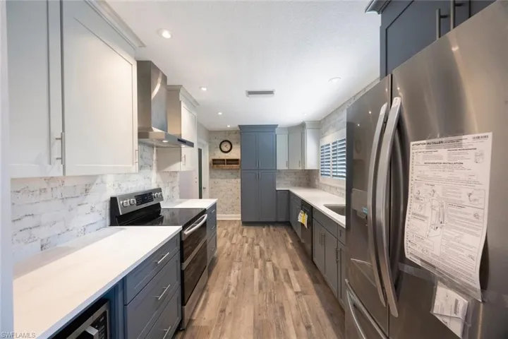 Kitchen featuring visible vents, stainless steel appliances, light countertops, wall chimney range hood, and backsplash
