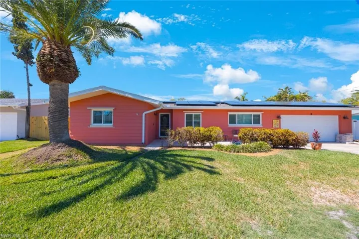 Ranch-style home with a garage, roof mounted solar panels, driveway, and a front yard