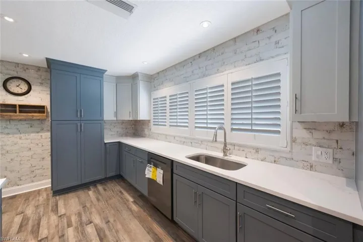 Kitchen featuring a sink, stainless steel dishwasher, wood finished floors, light countertops, and a healthy amount of sunlight