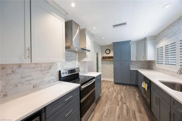 Kitchen with light countertops, wall chimney range hood, range with two ovens, and a sink