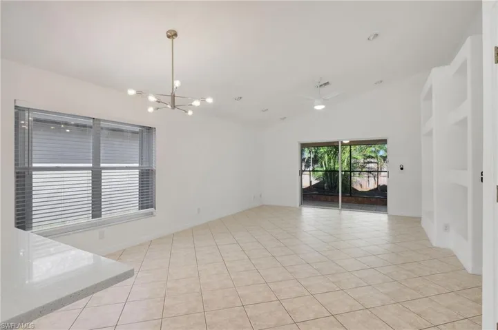 Empty room featuring lofted ceiling, light tile patterned floors, and ceiling fan with notable chandelier