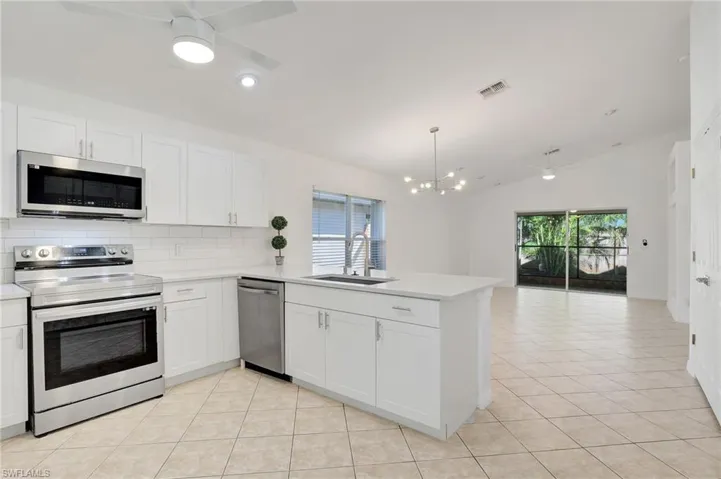 Kitchen with sink, appliances with stainless steel finishes, white cabinets, ceiling fan with notable chandelier, and kitchen peninsula