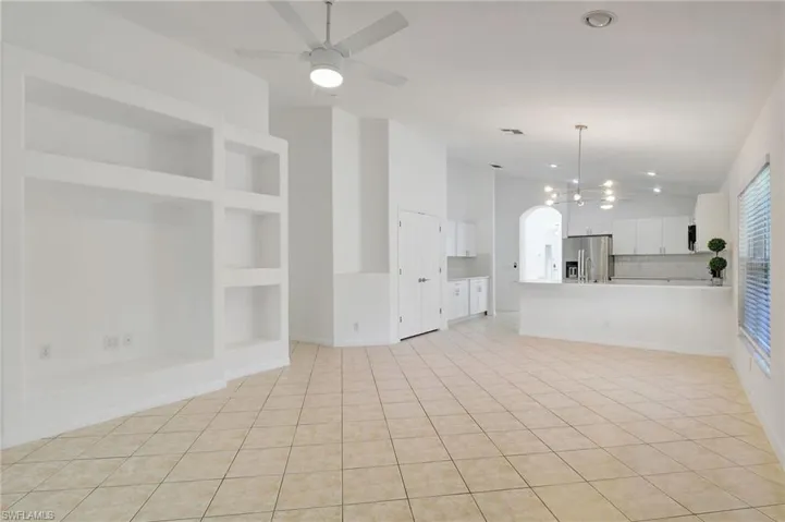 Unfurnished living room with light tile patterned floors, vaulted ceiling, built in features, and ceiling fan