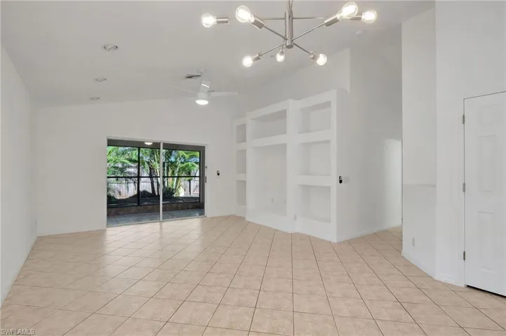 Unfurnished room featuring ceiling fan with notable chandelier, light tile patterned floors, built in features, and high vaulted ceiling