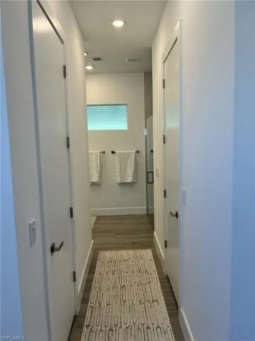 Hallway featuring wood-finish flooring, recessed lighting, and white paneled doors with dark hardware