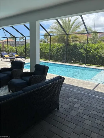 Screened outdoor living area featuring a rectangular pool with an integrated sun shelf, extensive paver decking, and lush perimeter landscaping