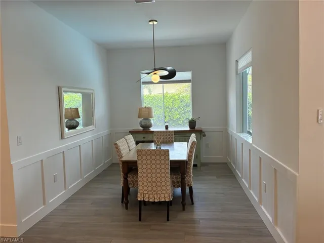 Spacious dining area featuring wood-finish flooring, white wainscoting, and large windows