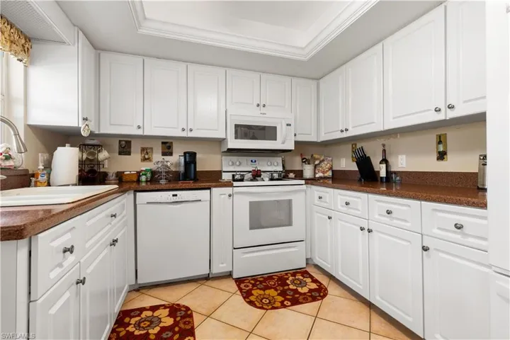 Kitchen featuring light tile patterned floors, white appliances, white cabinetry, sink, and a raised ceiling
