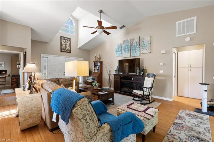 Living room with light hardwood / wood-style flooring, ceiling fan, high vaulted ceiling, and a fireplace