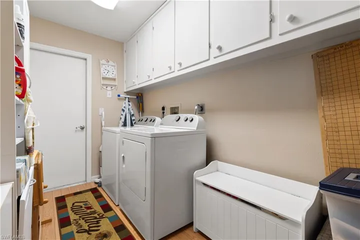 Washroom with light wood-type flooring, washing machine and clothes dryer, and cabinets