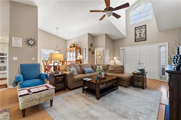 Living room with ceiling fan, high vaulted ceiling, and light hardwood / wood-style floors