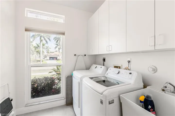 Clothes washing area featuring cabinets, sink, light tile patterned floors, and washing machine and clothes dryer