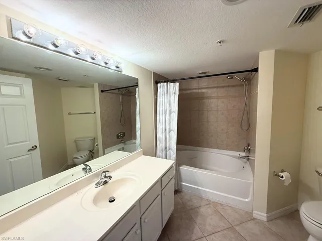 Full bathroom with shower / tub combo with curtain, vanity, a textured ceiling, and light tile patterned flooring