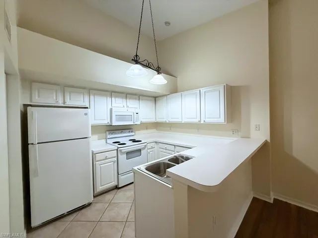 Kitchen featuring white appliances, a peninsula, pendant lighting, light countertops, and a towering ceiling