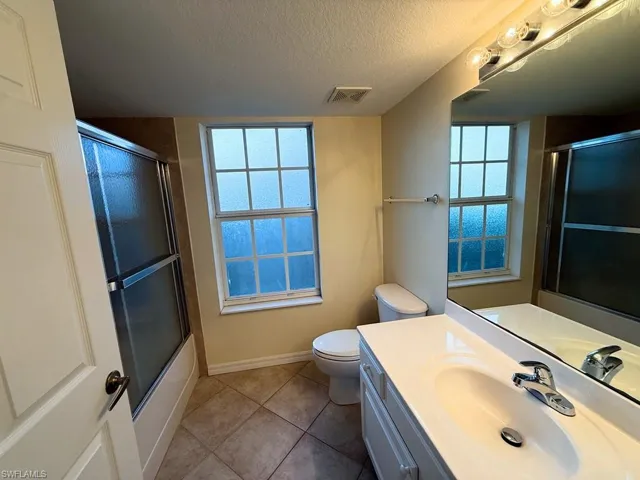 Full bathroom featuring vanity, a textured ceiling, light tile patterned floors, and bath / shower combo with glass door