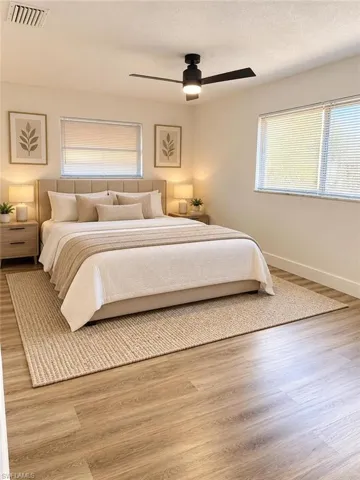 Neutral-toned bedroom featuring wood-finish flooring, dual windows with horizontal blinds, and a matte black ceiling fan with integrated lighting