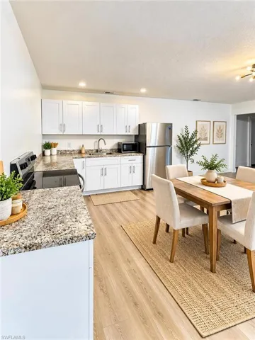 Kitchen featuring white shaker-style cabinetry, speckled stone-finish countertops, stainless steel refrigerator, recessed lighting, and wood-finish flooring