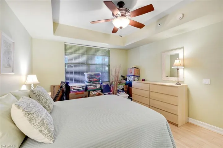 Bedroom with a raised ceiling, light wood finished floors, and ceiling fan