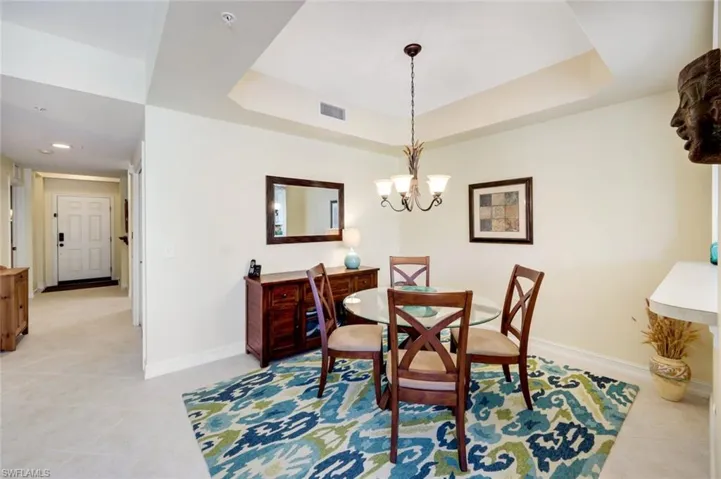 Dining space with a raised ceiling, light tile patterned flooring, and a chandelier
