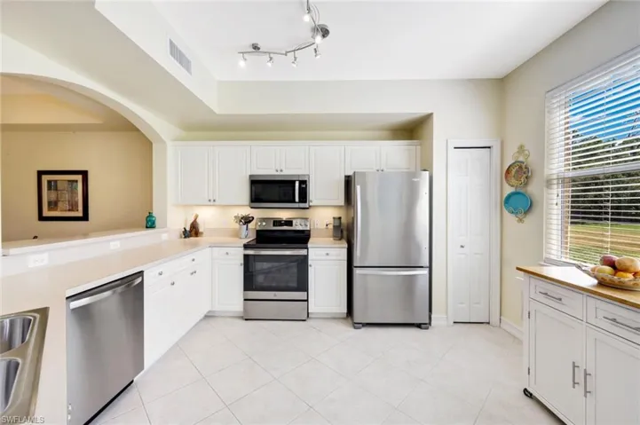 Kitchen with stainless steel appliances, light countertops, light tile patterned floors, and white cabinets