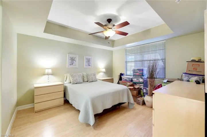 Bedroom with a raised ceiling, light wood-type flooring, and ceiling fan