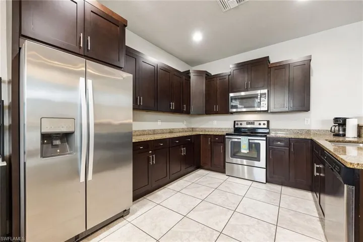 Kitchen featuring dark wood cabinetry, granite countertops, white tile flooring, and stainless steel appliances including a side-by-side refrigerator, range, microwave, and dishwasher