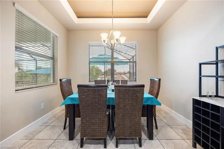 Recessed tray ceiling with central chandelier, tile flooring, and two large windows with blinds
