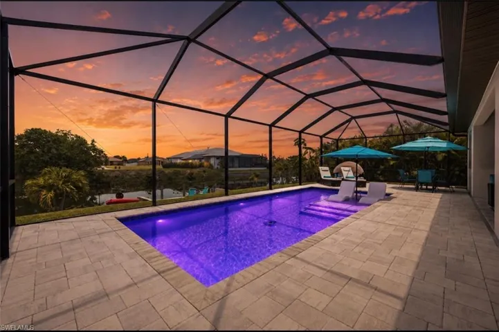 Screened lanai featuring a rectangular pool with integrated lighting, paver decking, and a stucco exterior wall