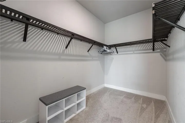Walk-in closet featuring built-in shelving, hanging rods, light gray walls, white baseboards, and neutral carpet flooring