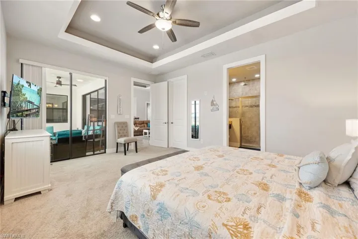 Spacious bedroom with light gray walls, plush carpet flooring, and a tray ceiling featuring recessed lighting and a ceiling fan
