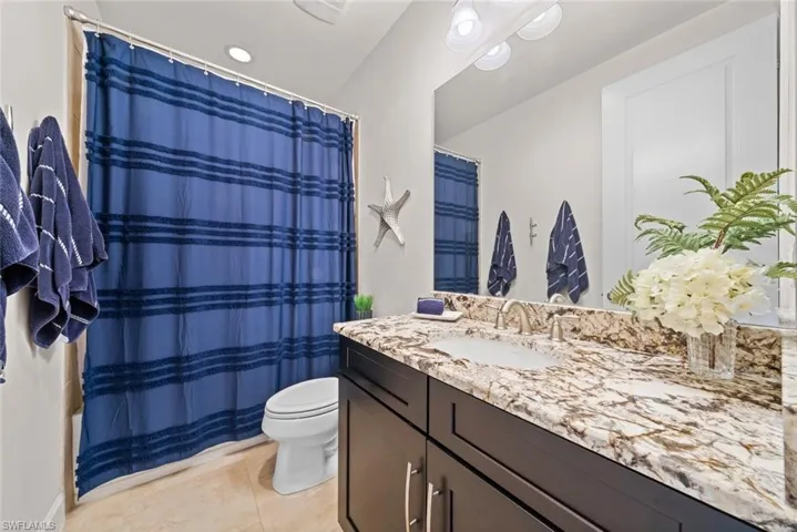 Bathroom featuring curtained shower, tile patterned flooring, vanity, and toilet