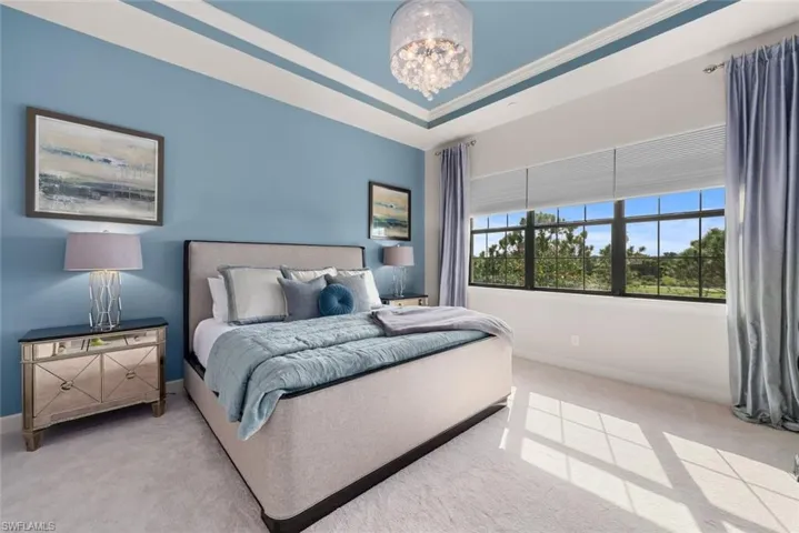 Carpeted bedroom with a raised ceiling, a chandelier, and ornamental molding