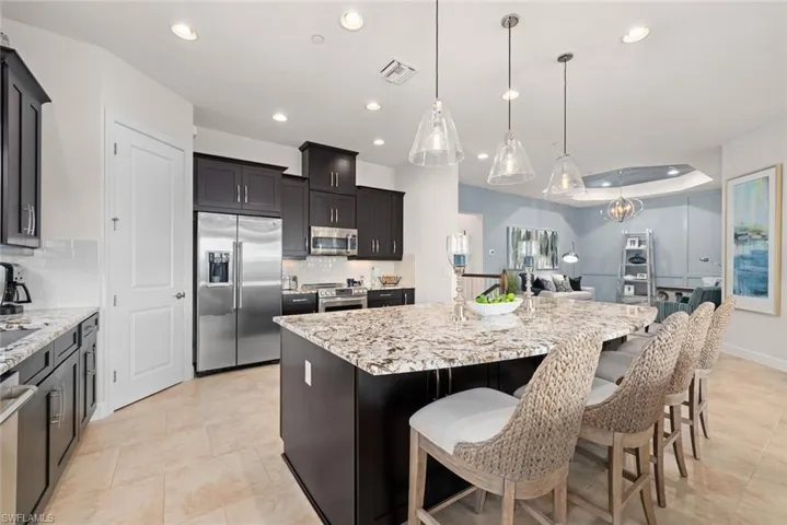 Kitchen featuring a kitchen bar, appliances with stainless steel finishes, a raised ceiling, a kitchen island with sink, and hanging light fixtures