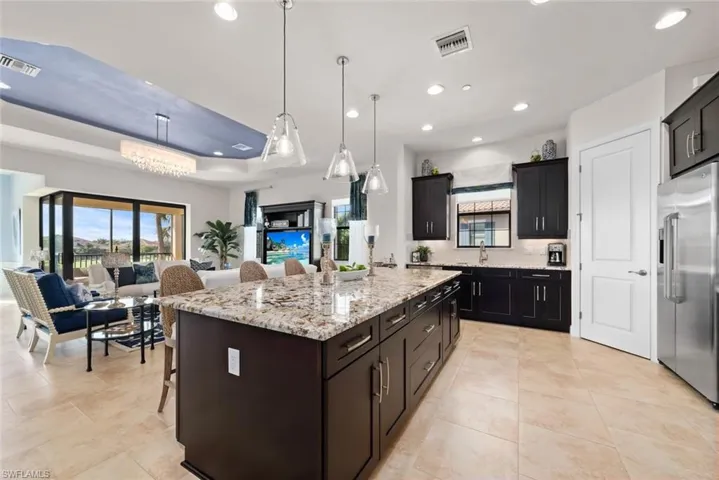 Kitchen with a kitchen breakfast bar, a raised ceiling, decorative light fixtures, high quality fridge, and a large island