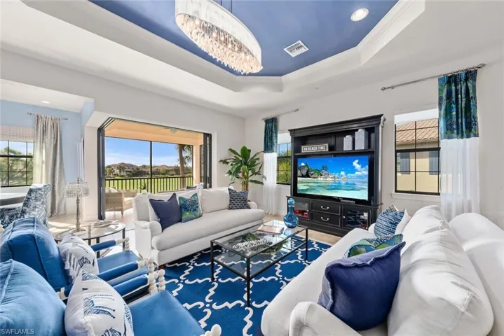 Living room with a tray ceiling, an inviting chandelier, plenty of natural light, and ornamental molding