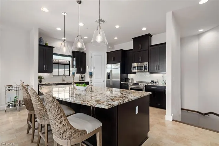 Kitchen with decorative backsplash, appliances with stainless steel finishes, light stone counters, a spacious island, and hanging light fixtures