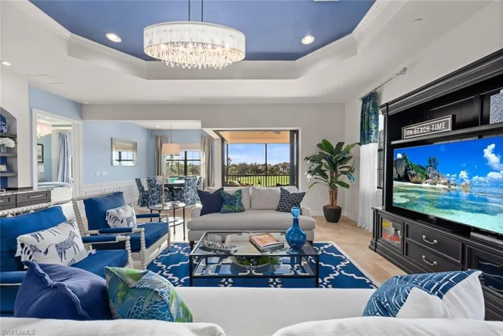 Living room with a raised ceiling, a notable chandelier, and ornamental molding