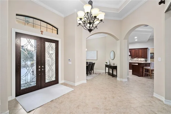Tiled entryway with a notable chandelier, ornamental molding, french doors, and a tray ceiling
