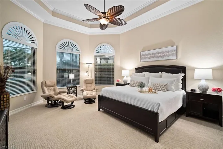 Carpeted bedroom with a raised ceiling, crown molding, and ceiling fan