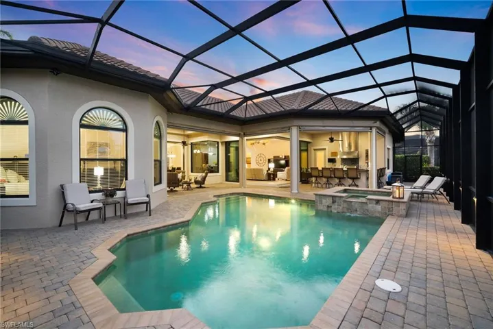 Pool at dusk with an in ground hot tub, screen enclosure, and a patio area