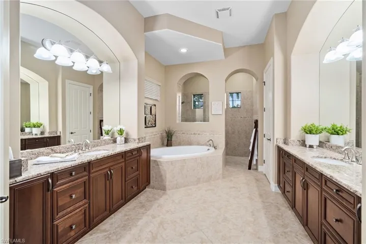 Bathroom featuring tile patterned flooring, tiled bath, and dual vanity