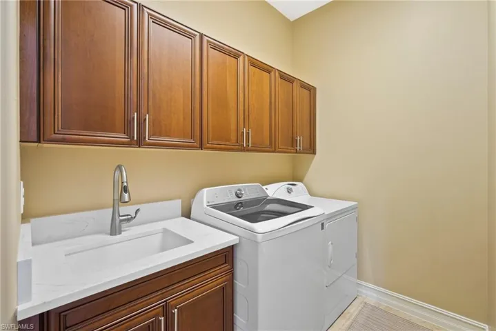 Laundry area with washer and clothes dryer, sink, cabinets, and light tile patterned floors