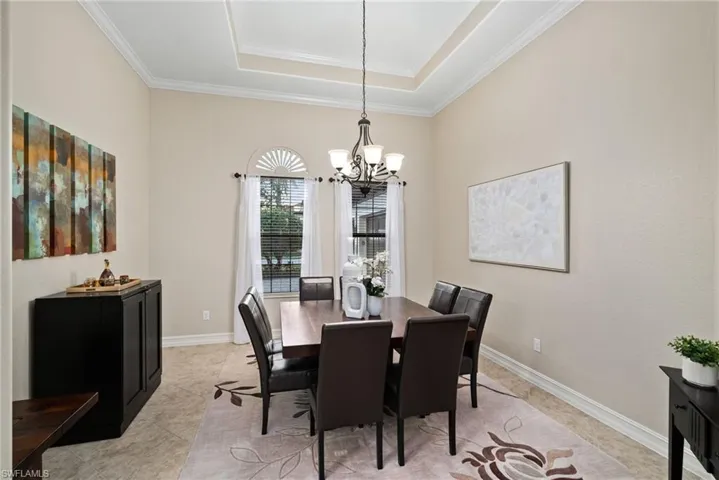 Tiled dining area with a raised ceiling, crown molding, and a notable chandelier