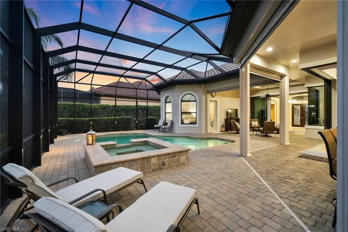 Pool at dusk featuring an in ground hot tub, a patio area, and a lanai