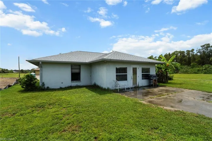 Back of house with stucco siding, a lawn, roof with shingles, and a patio