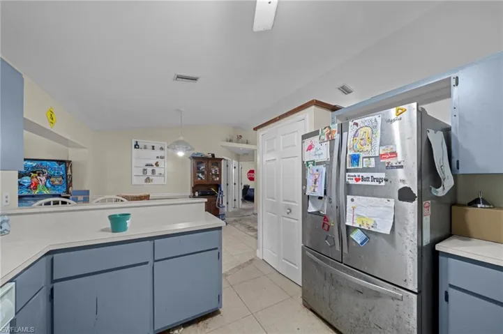 Kitchen featuring freestanding refrigerator, lofted ceiling, light countertops, light tile patterned floors, and decorative light fixtures