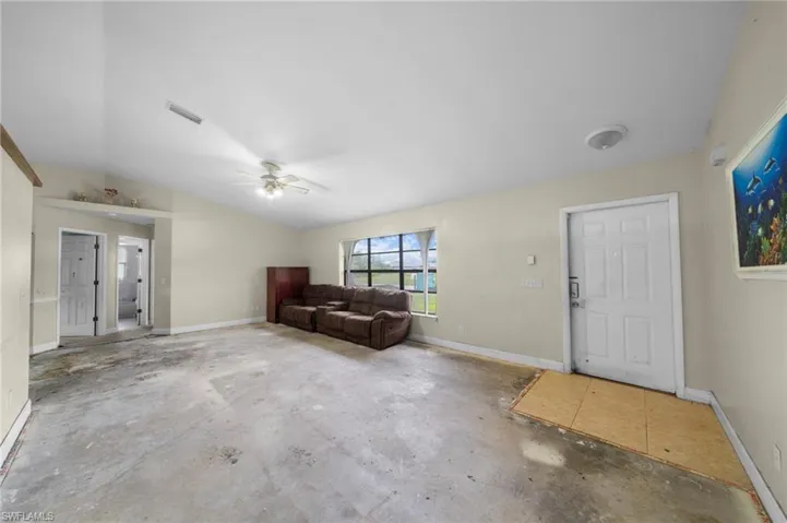 Foyer entrance with vaulted ceiling, a ceiling fan, and unfinished concrete floors