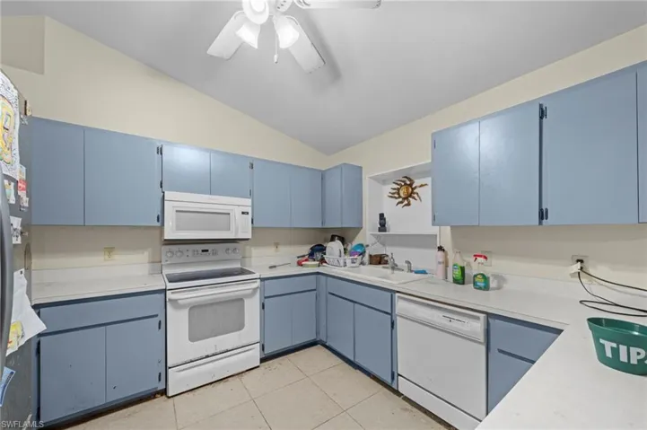 Kitchen featuring vaulted ceiling, blue cabinetry, white appliances, ceiling fan, and light countertops