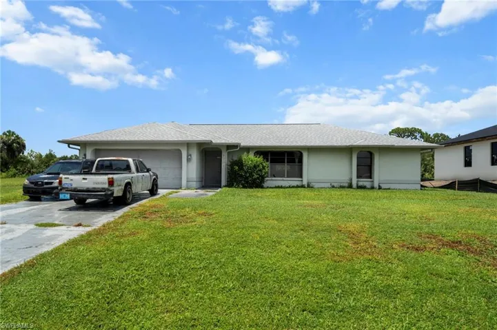 Ranch-style house featuring a garage, concrete driveway, stucco siding, and a front lawn