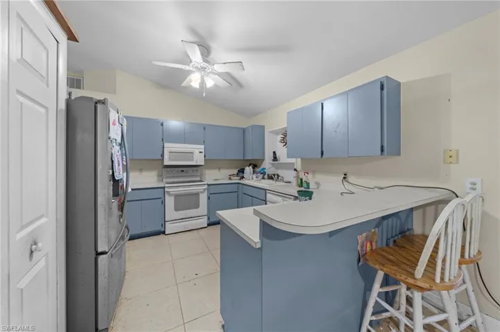 Kitchen featuring blue cabinets, a peninsula, lofted ceiling, white appliances, and light countertops